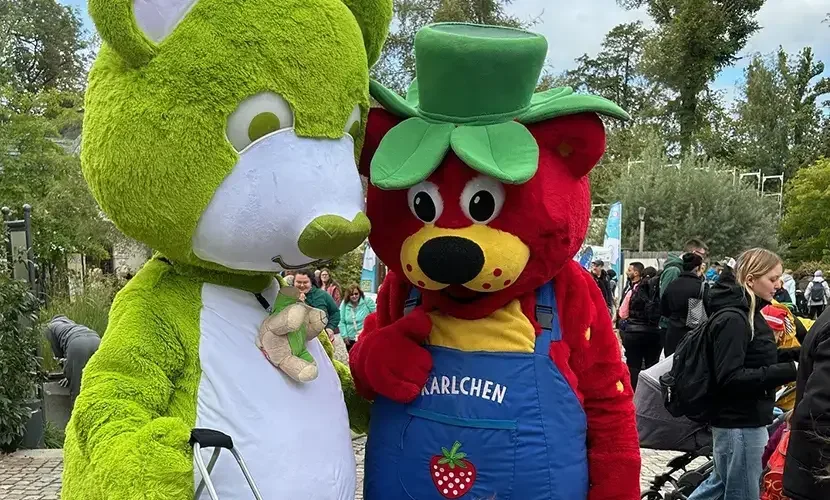 Grünes Kaninchenkostüm und rotes Bärenmaskottchen mit grünem Hut und blauer Latzhose mit Aufschrift „KARLCHEN“.