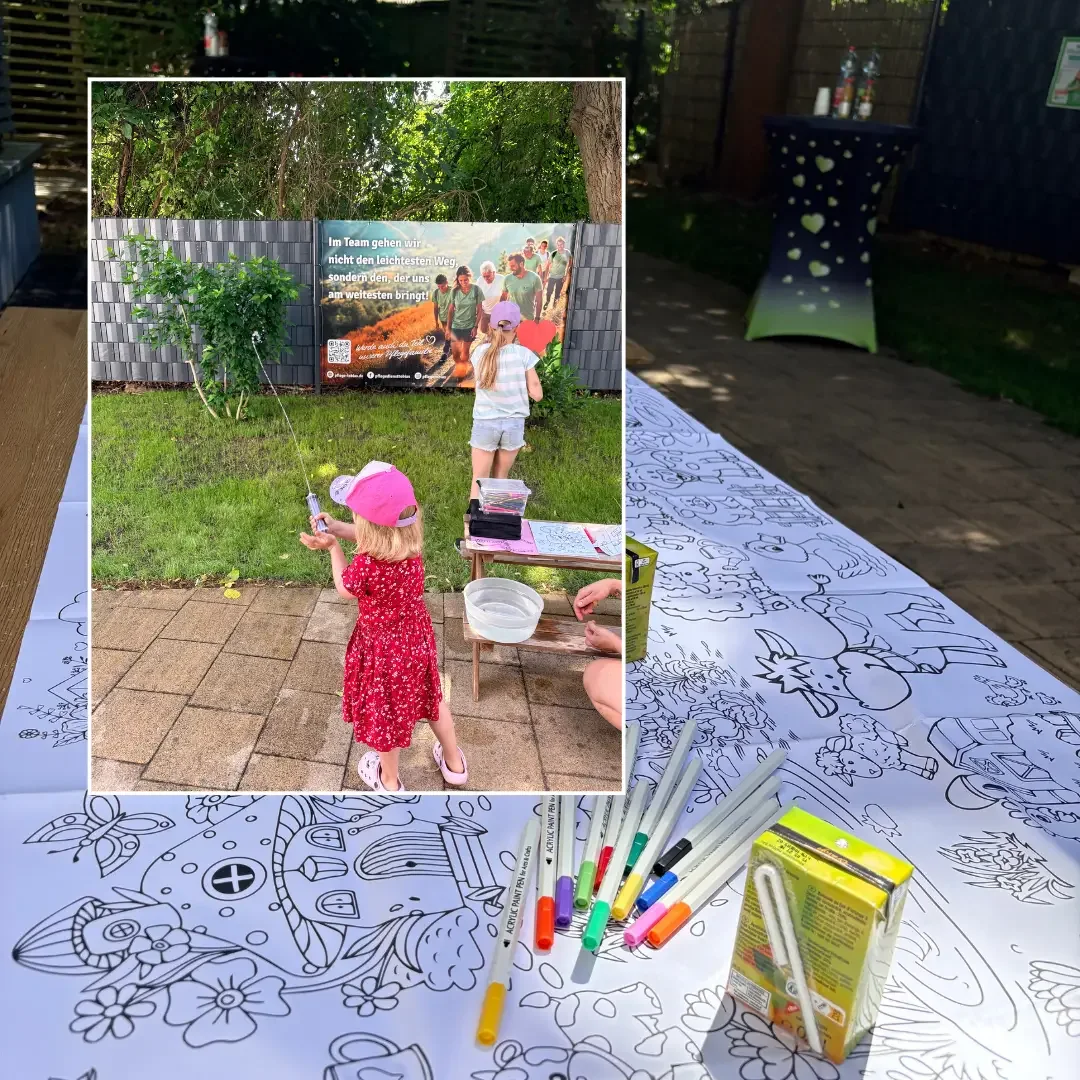 Langer Ausmaltisch mit Stiften im Garten, dazu Kinder vor einem Banner „Im Team gehen wir nicht den leichtesten Weg“.