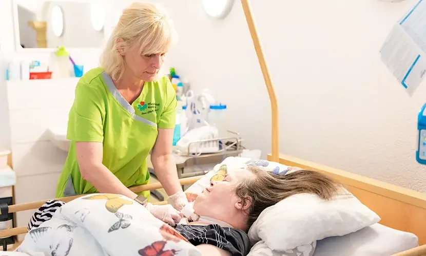 Pflegerin versorgt eine beatmete Frau im Pflegebett