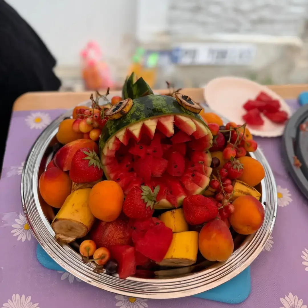 Silberne Platte mit Obst, in der Mitte eine als Fisch geschnitzte Wassermelone, umgeben von Erdbeeren und Aprikosen.