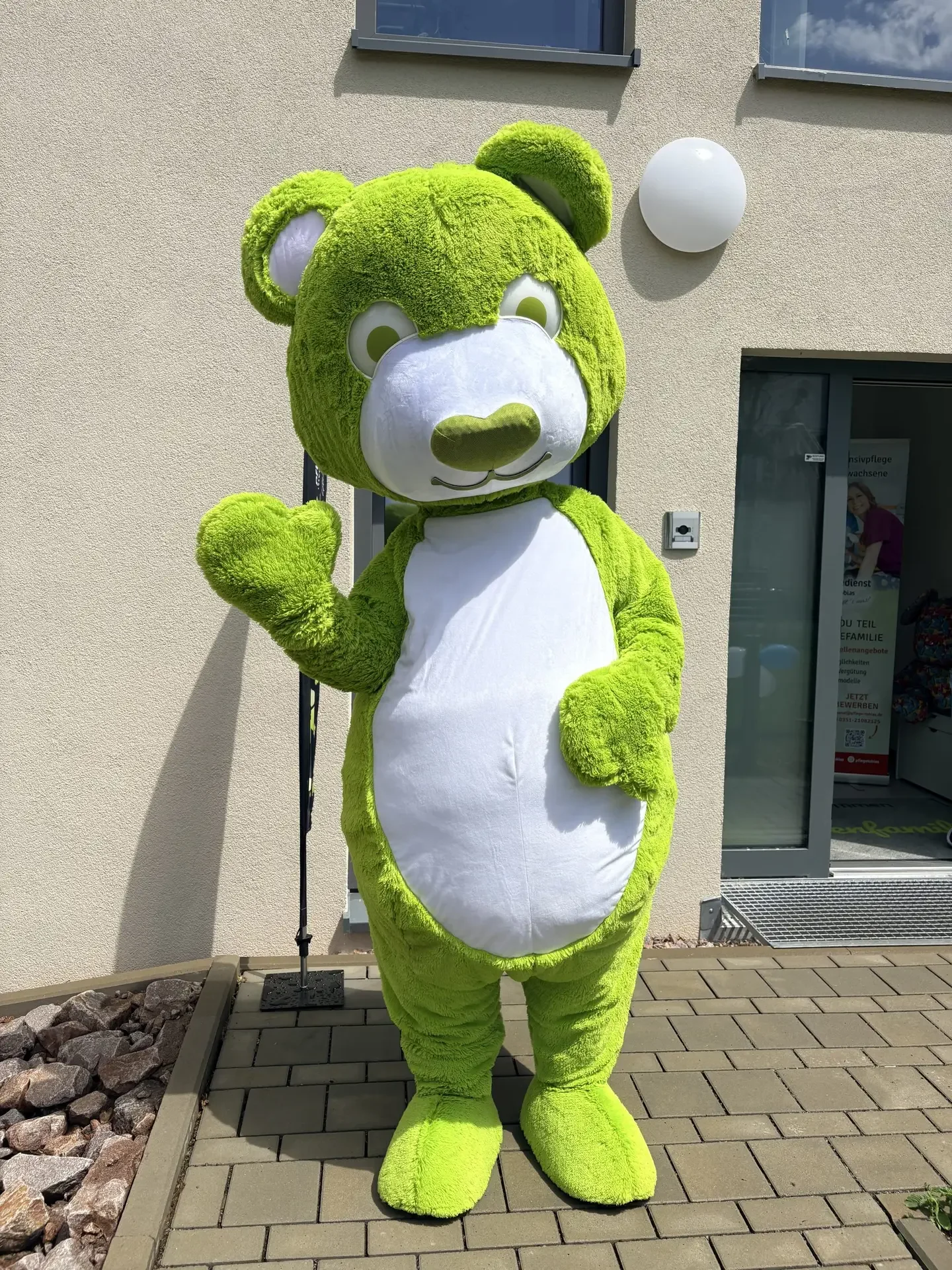 Grünes Bärenmaskottchen winkt vor dem Eingang der Leipziger Bärenfamilie